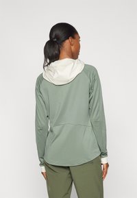 Maglia verde a maniche lunghe con cappuccio attaccato, realizzata in un tessuto leggero e con accenti beige a contrasto sul cappuccio e sui polsini.