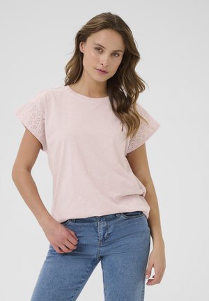 Lyserød kortærmet T-shirt med hulmønster på ærmerne, rund halsudskæring og en afslappet pasform. Sammen med blå jeans.