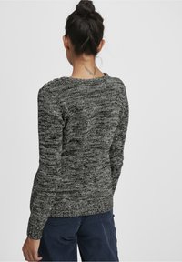 Pull en tricot gris avec un motif texturé, encolure ronde et poignets côtelés, porté avec un pantalon en velours côtelé bleu marine.