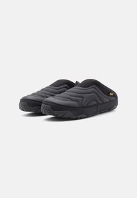 Fekete steppelt slip-on cipők párnázott felsőrésszel, texturált gumitalppal és arany színű minimális logóval az oldalon.