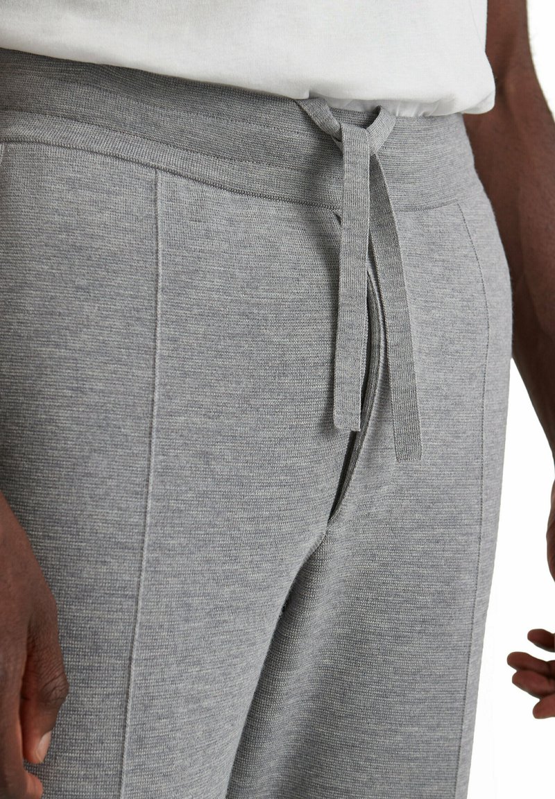 Grijze joggers zijn gemaakt van een gestructureerde stof, hebben een elastische tailleband en een verstelbaar treksnoer. Aan de zijkanten zijn zakken zichtbaar, met een relaxed fit ontwerp.