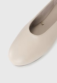 Beige läderballettskor med rund tå och mjukt tygfoder på en vit bakgrund.