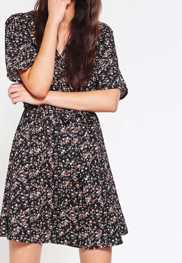 Robe noire à motifs floraux avec des manches courtes, un design portefeuille et un ourlet évasé. Le tissu a une apparence texturée et légère avec des fleurs multicolores.