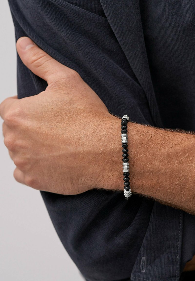 Bracelet en perles noires et argentées avec des formes géométriques, comportant des perles facettées noires alternées et des accents métalliques argentés.