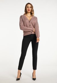 Cardigan roz deschis cu embellishments din rhinestone pe umeri, guler în V, nasturi negri, asortat cu pantaloni negri ajustați și tocuri.