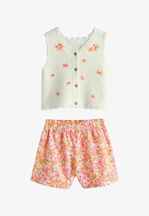 Kremowa dzianinowa kamizelka bez rękawów na guziki z różowymi i żółtymi haftowanymi kwiatami, zestawiona z różowo-pomarańczowo-białymi szortami w kwiatowy wzór.