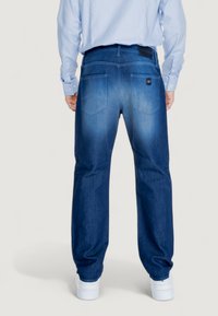 Jeans in denim blu scuro con taglio dritto, dotati di due tasche posteriori e una patch in pelle in vita, abbinati a sneakers bianche.