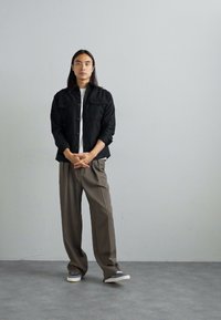 Black button-up shirt over white t-shirt, paired with gray wide-leg trousers and casual sneakers. Smooth textures and neutral tones.