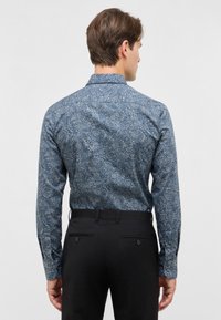 Camicia da uomo a maniche lunghe di colore blu scuro con motivo paisley. Presenta un colletto classico, polsini con bottoni e una vestibilità slim. Abbinata a pantaloni neri.