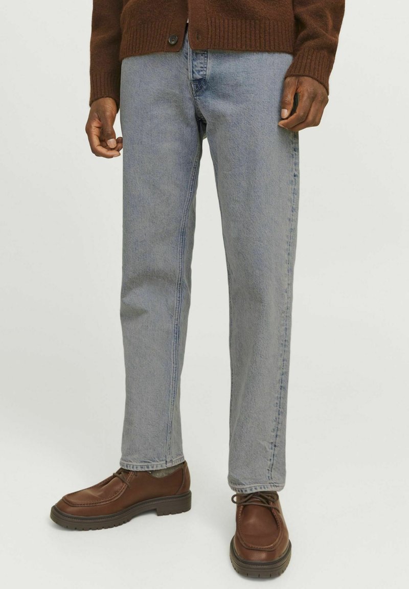 Jeans de mezclilla azul claro con un corte recto, que presentan un diseño clásico de cinco bolsillos, combinados con zapatos de cuero marrón y un suéter marrón oscuro.