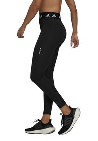 Svarta sportleggings med hög midja, utrustade med en vit logotyp och ett grått mönster. Bärs med svarta löparskor.