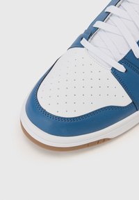 Blue and white leather sneaker with perforated toe, round toe shape, white laces, and gum rubber sole. Smooth texture with contrasting accents.