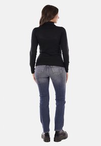 Maglione a collo alto nero in maglia abbinato a jeans blu. L'outfit presenta un design aderente e orli a costine, completato da calzature nere robuste.