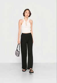 Top halter branco canelado com frente em formato de olho-chave, combinado com calças largas pretas. Acessórios incluem uma mala em mármore preto e cinza.