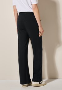 Zwarte, wijde broek van zacht materiaal met een elastische tailleband en twee achterzakken. Gladde textuur en vloeiende ontwerp.