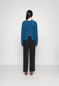 Suéter azul tricotado com corte oversized, recorte nas costas e gola canelada. Combinado com calças pretas de cintura alta e sapatos de salto com tiras.
