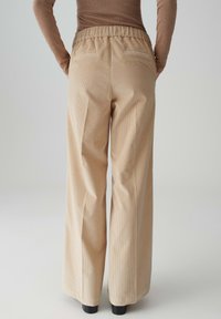 Pantaloni a gamba larga in corduroy beige con superficie testurizzata, vita elasticizzata e due tasche posteriori, mostrati da dietro.