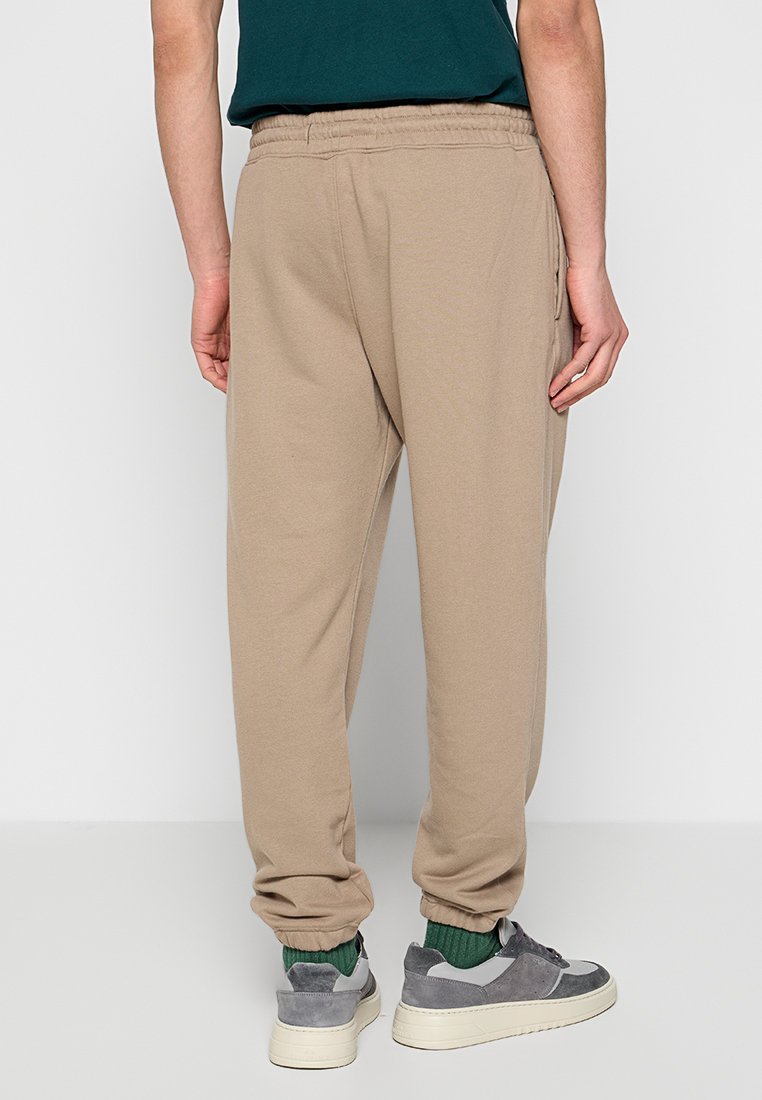 Beżowe spodnie dresowe wykonane z miękkiej tkaniny, z ściągaczami na kostkach i elastycznym paskiem w talii. Widoczne detale w postaci szwów oraz boczne kieszenie.