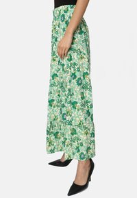 Jupe maxi florale verte avec un design à étages et une taille élastique ; présente différentes nuances de vert et des touches de violet sur un fond clair.