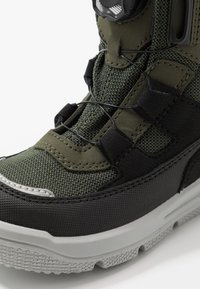 Sneaker verde e nero con tomaia in tessuto, suola in gomma testurizzata e sistema di allacciatura. Presenta punta rinforzata e dettagli testurizzati.