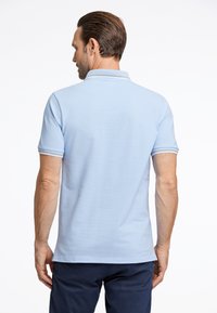 Camisa polo azul cielo con cuello clásico, mangas cortas y detalles a rayas en los puños. Tejido texturizado con un acabado suave.