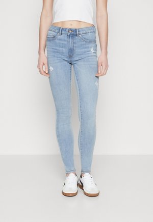 Light blue skinny jeans with distressed detailing, made of denim, feature a mid-rise waist and slim fit, paired with white sneakers.