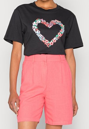 Zwart T-shirt met een hartvormig bloemenpatroon, gecombineerd met hooggesneden, losvallende shorts in koralen roze.