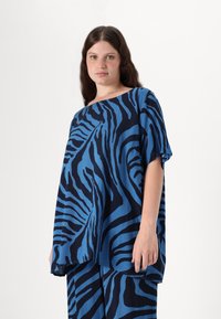 Zila un melna zebrām līdzīga raksta blūze, brīva piegriezuma, īsām piedurknēm, apaļš kakla izgriezums, izgatavota no mīkstas auduma, gluda tekstūra, maigi krīt.
