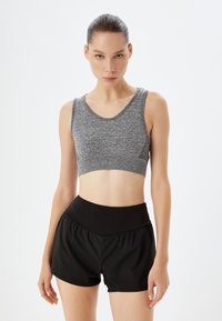 Grå crop top med en tekstureret finish og bred udskæring, parret med højtaljede sorte træningsshorts med samling.