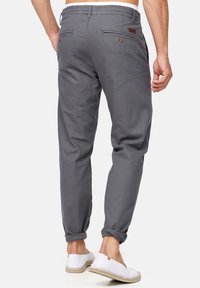 Graue Baumwollhosen mit umgeschlagenen Säumen, ausgestattet mit zwei Gesäßtaschen mit braunen Knöpfen und einem dezenten Logo-Detail am Bund.