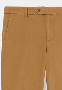 Beige Hosen mit Seitentaschen, Gürtelschlaufen und einem Knopfverschluss am Bund, von der Taille bis zur Mitte des Oberschenkels gezeigt.