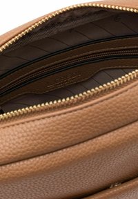 Interior de bolsa de cuero texturizado marrón con compartimentos con cremallera y herrajes dorados. Forrada con tela rayada y detalle de logo en relieve.