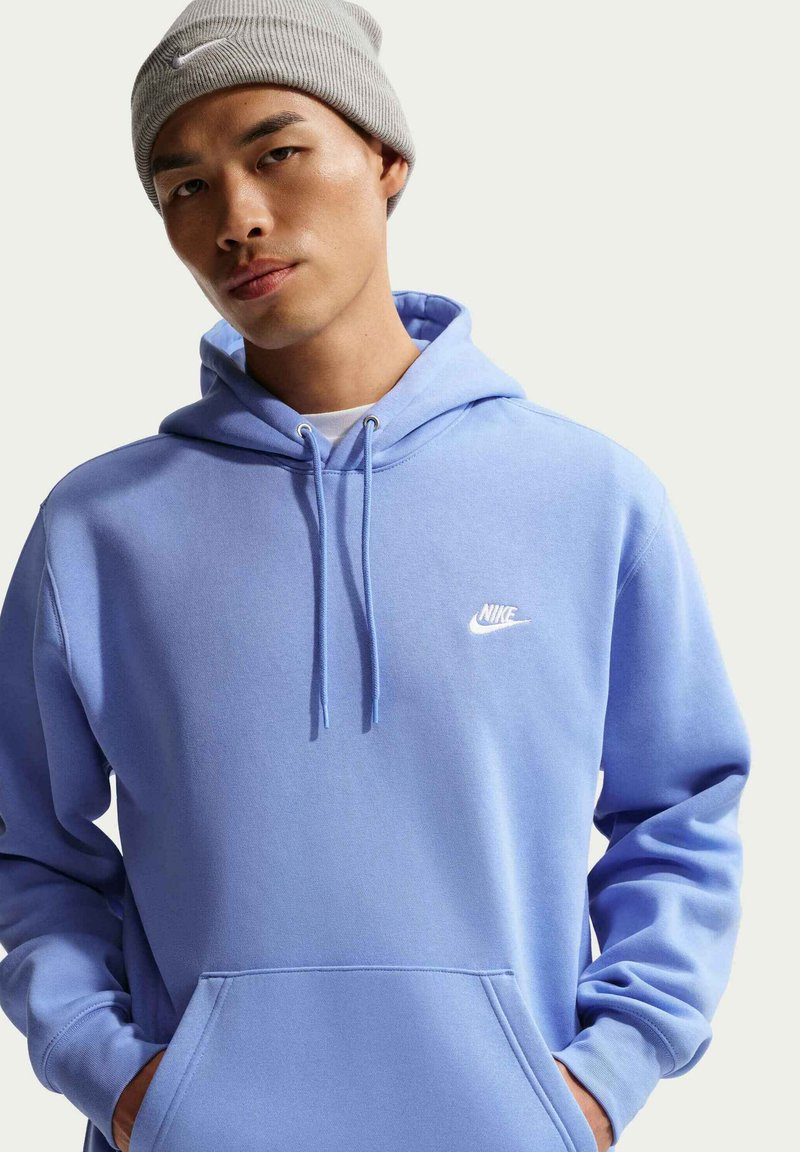 Sudadera con capucha Nike azul claro con bolsillo frontal, capucha ajustable con cordón y logo blanco en el pecho; combinada con un gorro de punto gris acanalado.