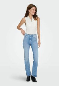 Balta be rankovių palaidinė su užtrauktuku, derinama su šviesiai mėlynomis aukštu juosmeniu džinsais. Aprangą pabrėžia juodi auliniai batai iki kulkšnies.