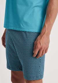 Turquoise shirt met korte mouwen, gecombineerd met marineblauwe zwemshorts met een geometrisch lichtblauw driehoekpatroon. Gladde stof, casual fit.
