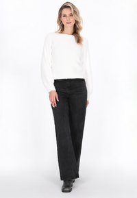 White textured sweater with long sleeves, paired with high-waisted black wide-leg jeans. The outfit is complemented by black boots.