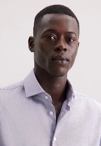 Camicia aderente a maniche corte di colore viola chiaro con motivo a griglia. Presenta un colletto con bottoni e bottoni bianchi. Tessuto liscio e intrecciato.