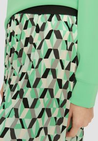 Jupe imprimée présentant des motifs géométriques dans des teintes de vert menthe, noir et gris. Tissu lisse avec une taille élastique noire.