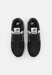 Black sneakers with mesh and suede materials, featuring white accents, a textured sole, and prominent New Balance logo and model number 574.