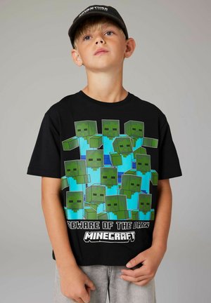 T-shirt nera con personaggi pixelati verdi e accenti blu, testo "Attenti al Buio" e "Minecraft" in bianco nella parte inferiore.