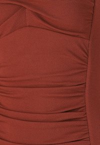 Tissu rouge texturé avec un motif en nid d'abeille, présentant des sections froncées et des panneaux lisses pour un design structuré.