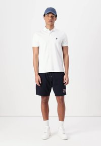 White polo shirt with short sleeves, navy shorts, and white sneakers. Accessorized with a light blue cap, featuring a logo detail.