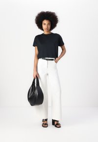 Camiseta negra de cuello redondo, pantalones anchos blancos, cinturón negro, bolso hobo negro y sandalias de tacón cuadrado negro con detalles dorados.