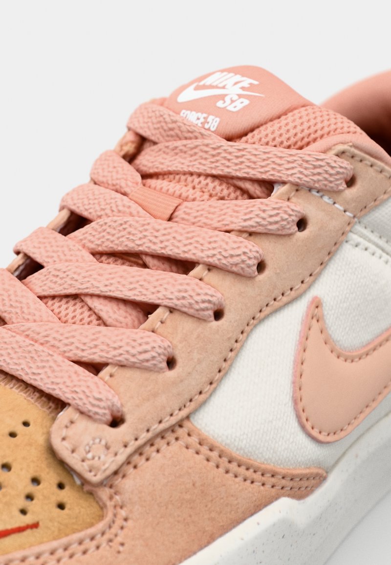 Las sneakers Nike SB cuentan con una parte superior de ante rosa y beige, cordones de textura rosa, toques de lona blanca y un logotipo de swoosh reconocible.