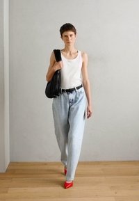 Sac en cuir noir plissé, débardeur blanc, jeans bleu clair taille haute, escarpins rouges à bout pointu, fond minimaliste avec un sol en bois.