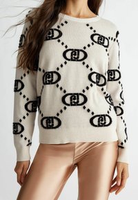 Beiger Pullover mit schwarzen, flauschigen geometrischen Mustern und einem gerippten Saum. Lange Ärmel mit Rundhalsausschnitt. Akzentuierte Textur und Design.