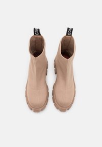 Bottines beiges jusqu'à la cheville avec une tige en tricot extensible, surface texturée et semelle en caoutchouc épaisse. Présente un tirette noire au niveau du talon.