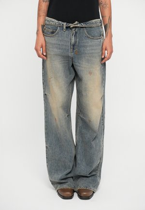 Laiad jaladest denim püksid pleekinud sinises värvitoonis, millel on kulunud välimus. Kinnitatud nööbi ja vöökummiga, samuti on jalgadel plaastritega detailid.