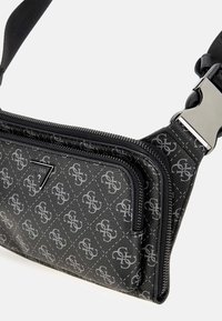 Bolso bandolera negro hecho de material sintético texturizado, presenta un patrón de logotipos, herrajes plateados y dos compartimentos con cremallera.