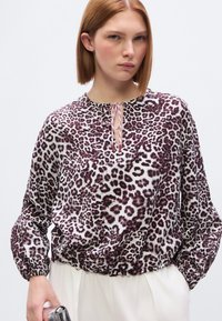 Μπλουζάκι με μοτίβο λεοπάρ σε μοβ και λευκό χρώμα, με μακριά φουσκωτά μανίκια και ελαστικό τελείωμα. Διαθέτει άνοιγμα στο μπροστινό μέρος με δέσιμο.